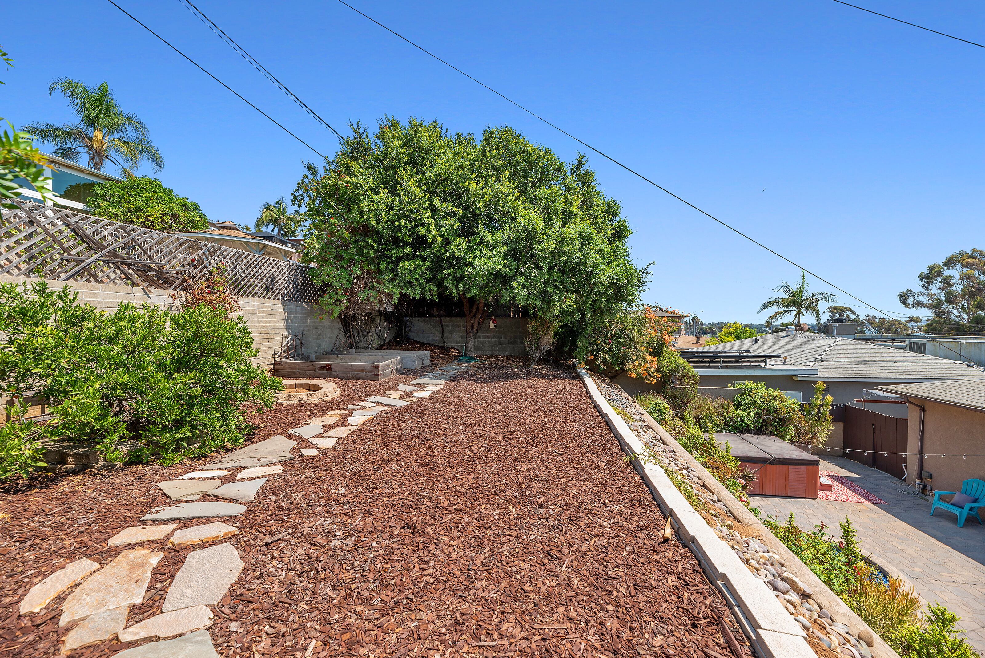 A backyard with a stone pathway, a tree, and a patio area with a shed and outdoor furniture.