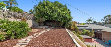 A backyard with a stone pathway, a tree, and a patio area with a shed and outdoor furniture.