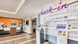 Een hotel receptie met een incheckautomaat, een digitaal scherm en een muur met motiverende citaten.