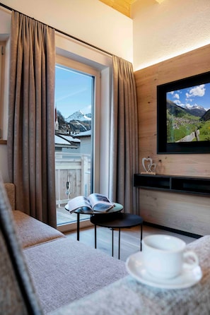 A room with a large window, a television, a cup on a table, and a view of mountains.