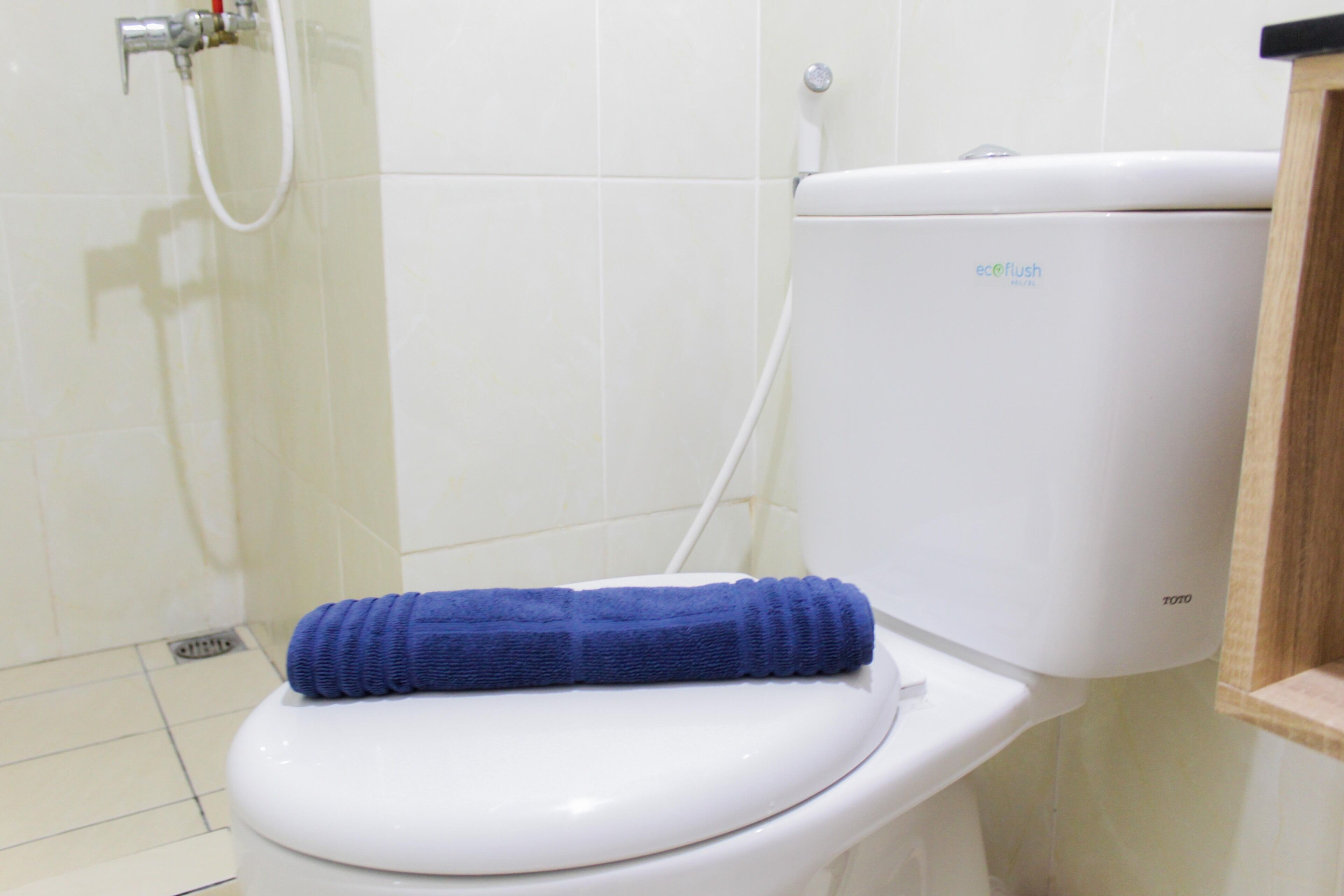 Inodoro blanco con una toalla azul sobre el asiento y un tanque de agua con la etiqueta 'eco flush' al fondo.