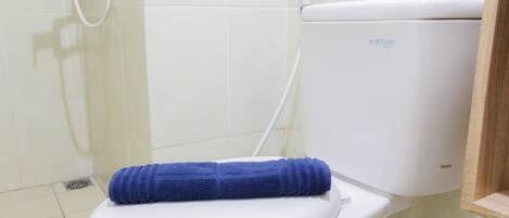 Inodoro blanco con una toalla azul sobre el asiento y un tanque de agua con la etiqueta 'eco flush' al fondo.