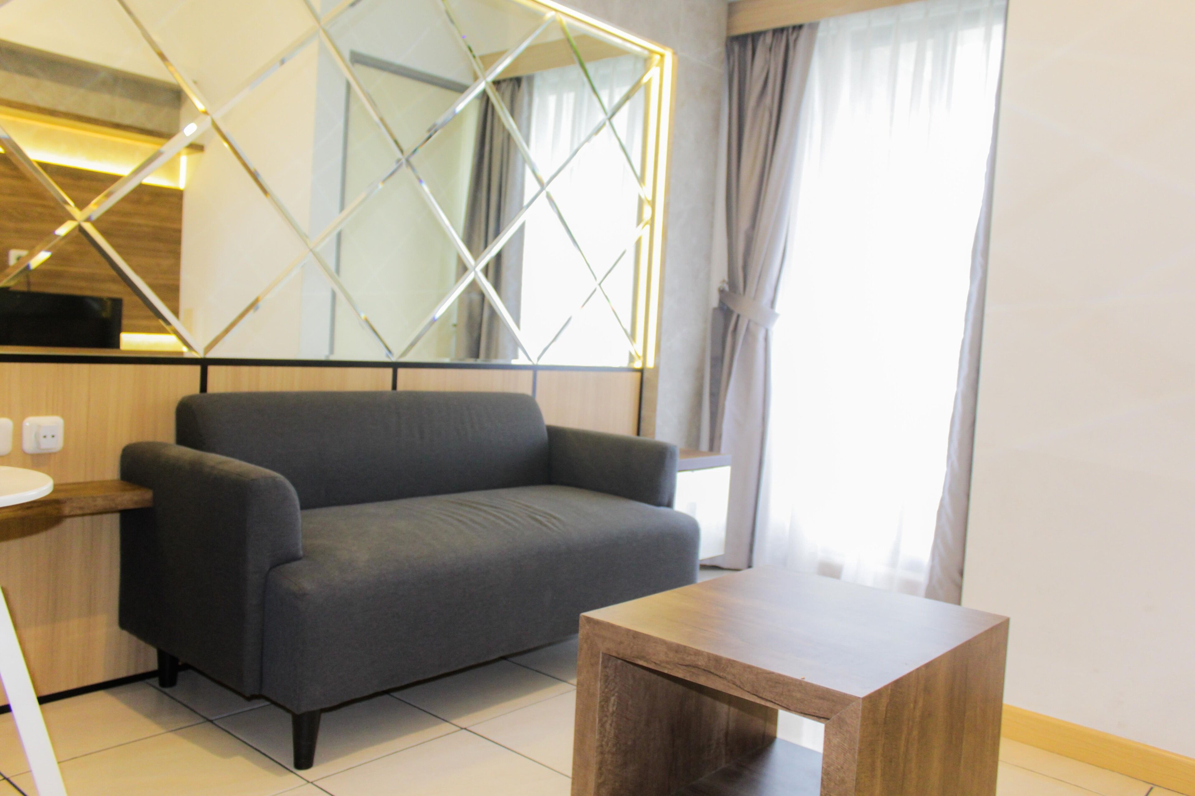 A modern living room with a grey sofa, a wooden coffee table, and a large mirror with a geometric frame.