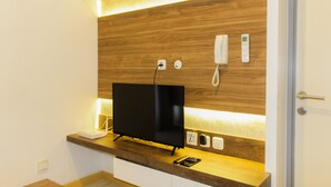 A modern hotel room with a wooden accent wall, a flat-screen TV, a bedside table, and a bedside lamp. - Modern and Clean 2BR Apartment at M-Town Residence (Gading Serpong)