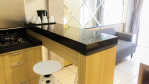 A compact kitchen with a gas stove, a coffee maker, and a small white stool. - Modern and Clean 2BR Apartment at M-Town Residence (Gading Serpong)