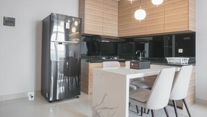 A modern kitchen with a stainless steel refrigerator, wooden cabinets, a black microwave, and a white dining table with chairs.