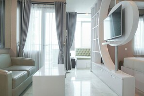 A modern living room with a sofa, a coffee table, and a TV mounted on a white wall. - Premium and Spacious Studio Apartment at Capitol Park Residence (Jakarta)