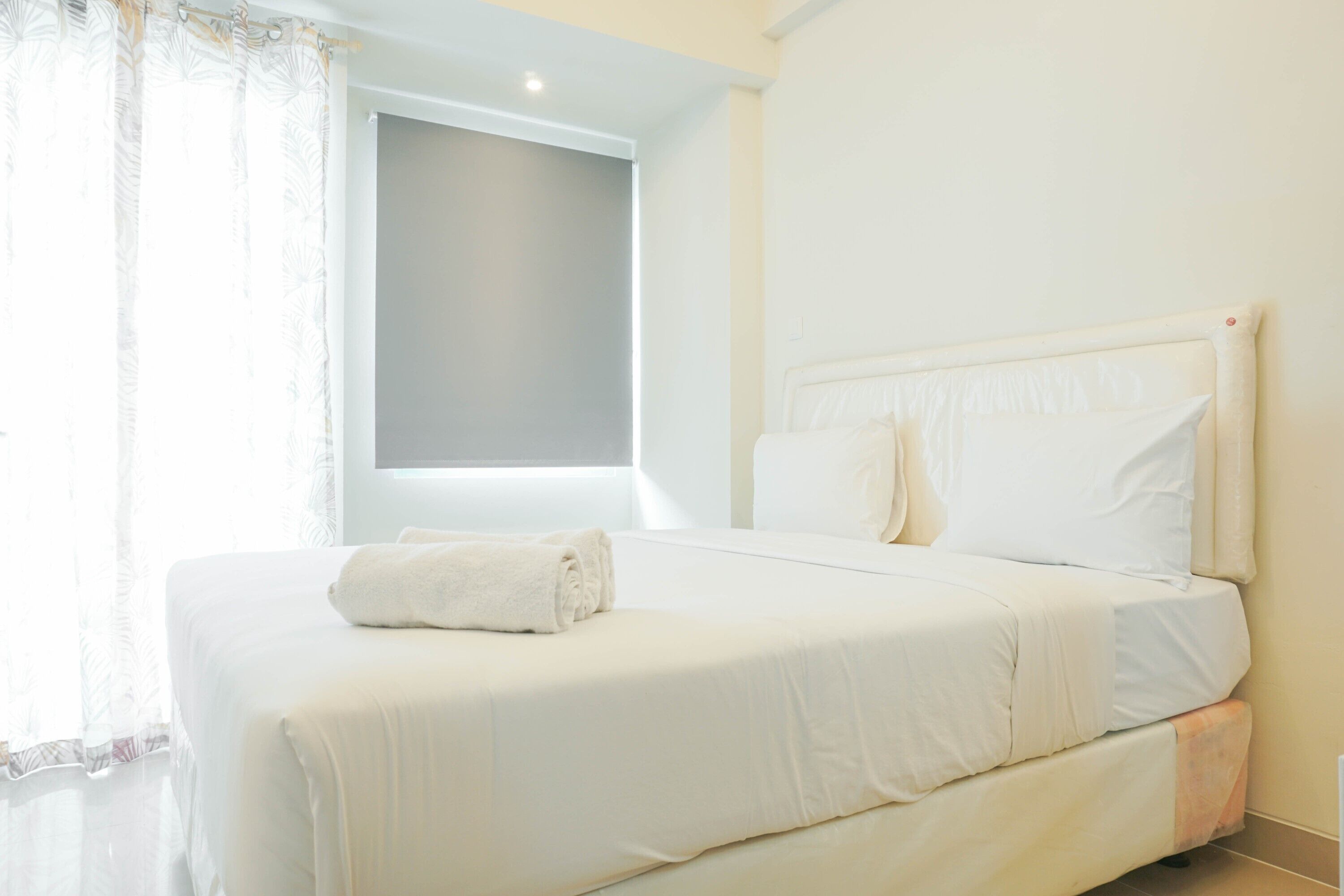 Une chambre d’hôtel avec un grand lit, une fenêtre avec des rideaux et un mur sobre.