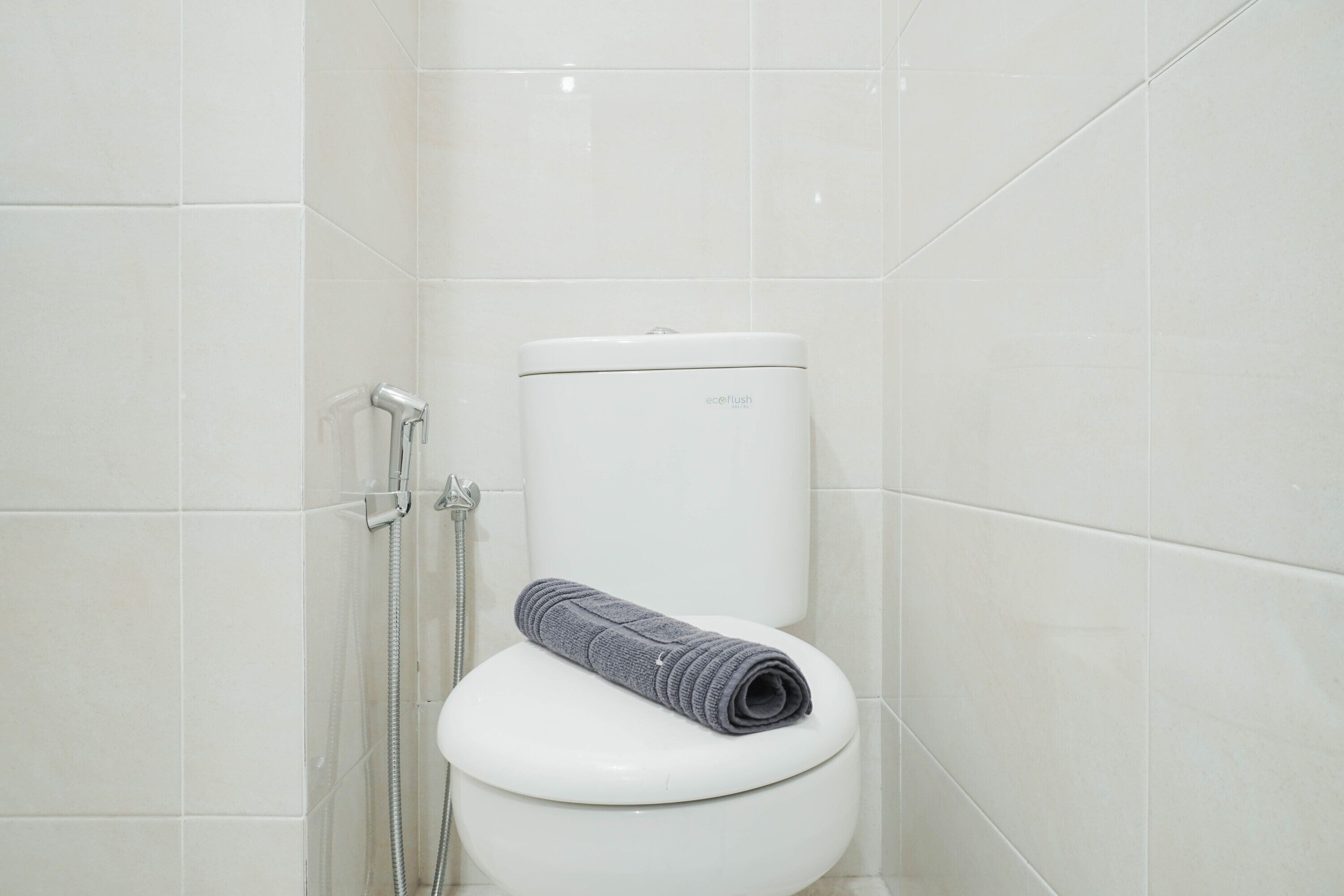 A white toilet with a grey towel on top, a handheld showerhead, and a toilet paper holder.
