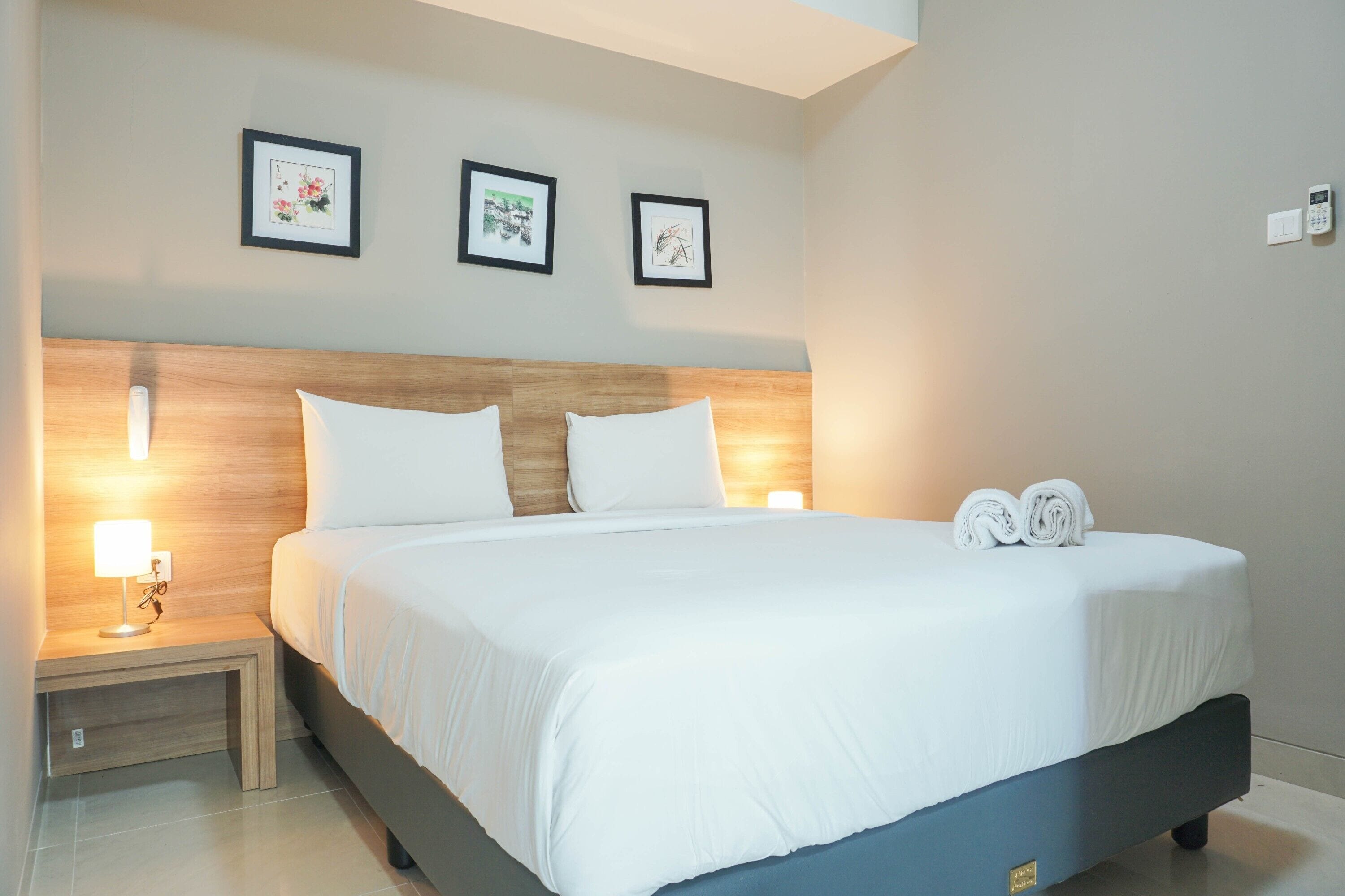 A neatly made bed with white linens, a wooden headboard, and two framed pictures on the wall above.