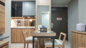 A compact kitchen with wooden cabinets, a glass-top dining table, and a coffee machine. - Elegant 1BR Apartment with Working Space Mustika Golf Residence (Cikarang)