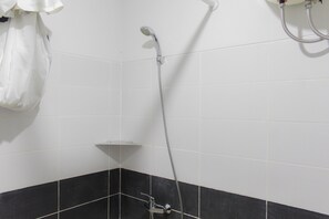 Shower and bathtub area features a showerhead with a flexible hose and a wall-mounted shelf.