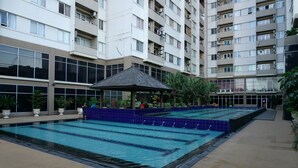 Zona de piscina con un pabellón, rodeada por un edificio residencial de varios pisos con balcones y ventanas amplias.