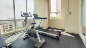 Ein Fitnessraum mit Laufband und Crosstrainer, großen Fenstern mit Blick auf die Stadt und einem kleinen Fenster mit Grünpflanzen.