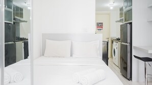 Moderni hotellihuone, jossa on siististi pedattu sänky, pieni keittokomero ja pesukone taustalla.