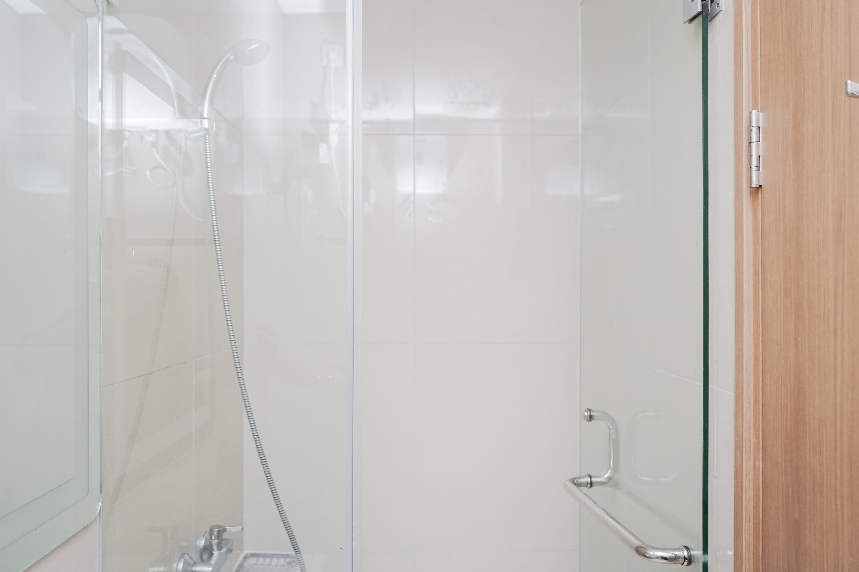 A glass-enclosed shower with a handheld showerhead and a control panel.