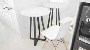 A modern kitchen with white cabinets, two round tables with black legs, and a white chair.