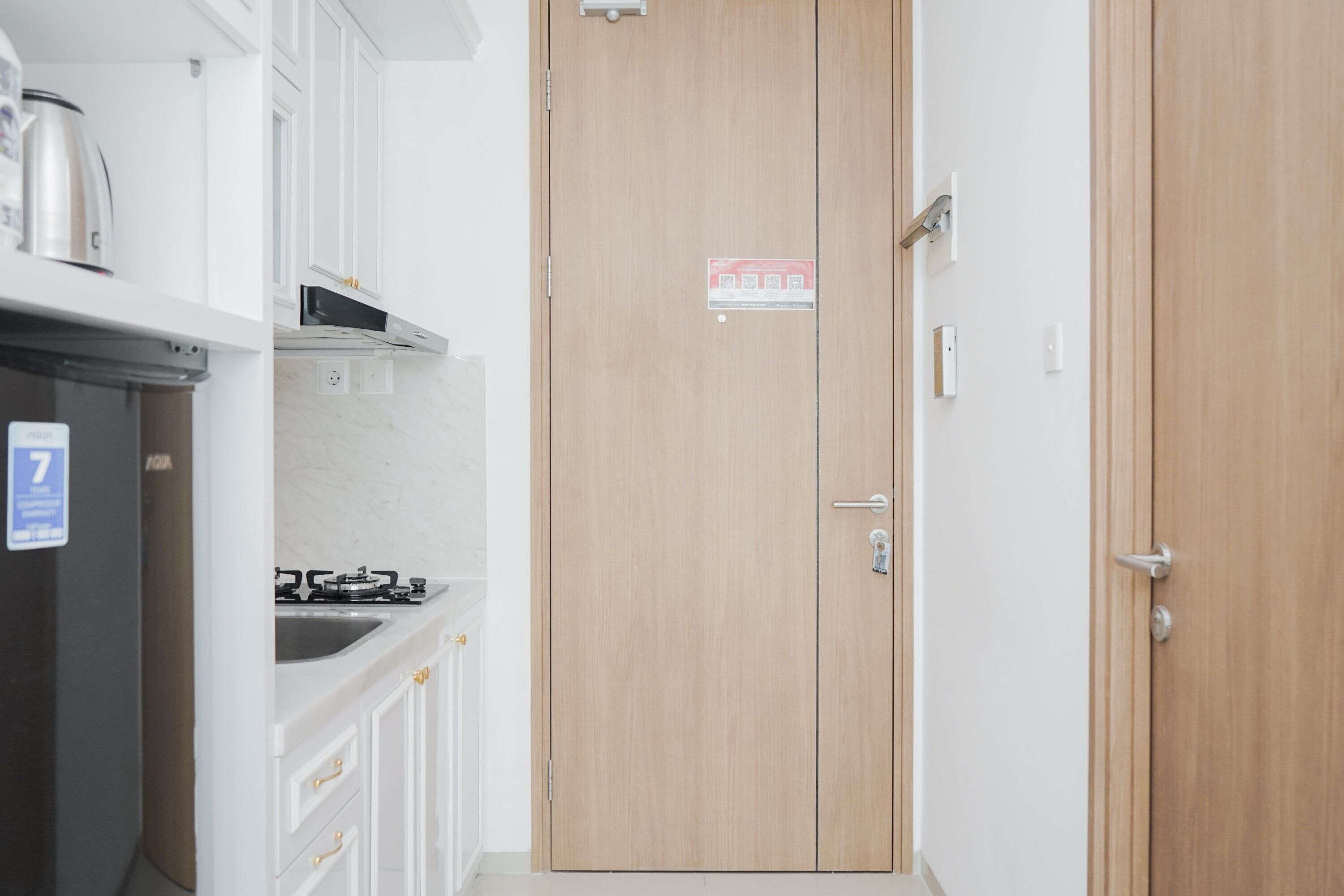 Cocina compacta con armarios blancos, hervidor de acero inoxidable y cocina a gas.
