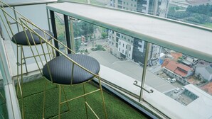 A balcony with two black cushioned chairs and a glass railing overlooking a cityscape.