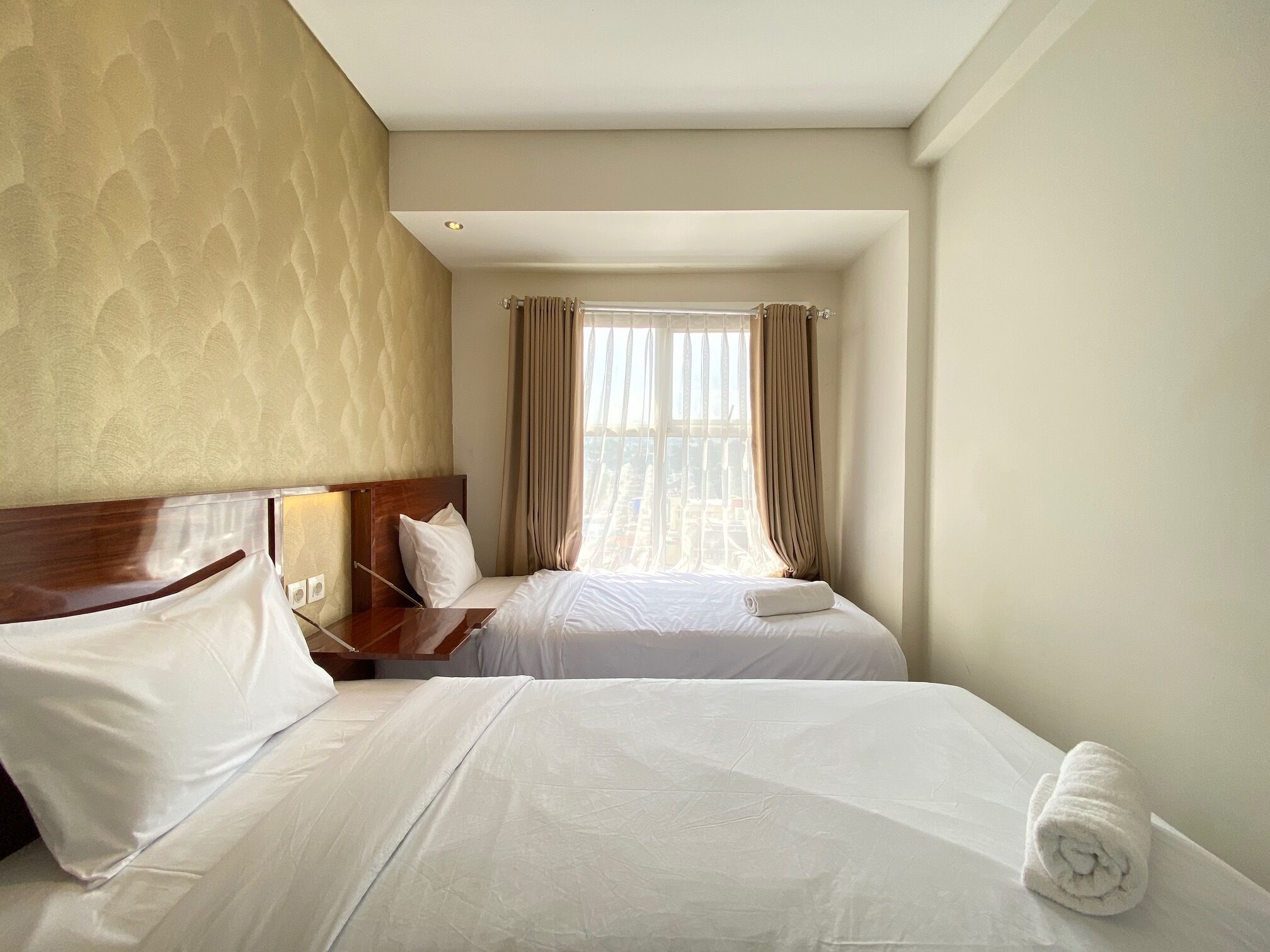 A hotel room with two beds, a wooden headboard, a window with curtains, and a city view.