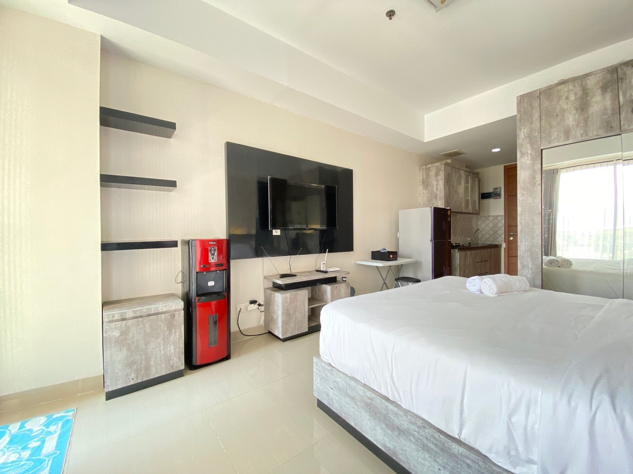 Een moderne hotelkamer met een groot bed, een flatscreen televisie aan de muur, een minibar en een klein bureau met stoel.
