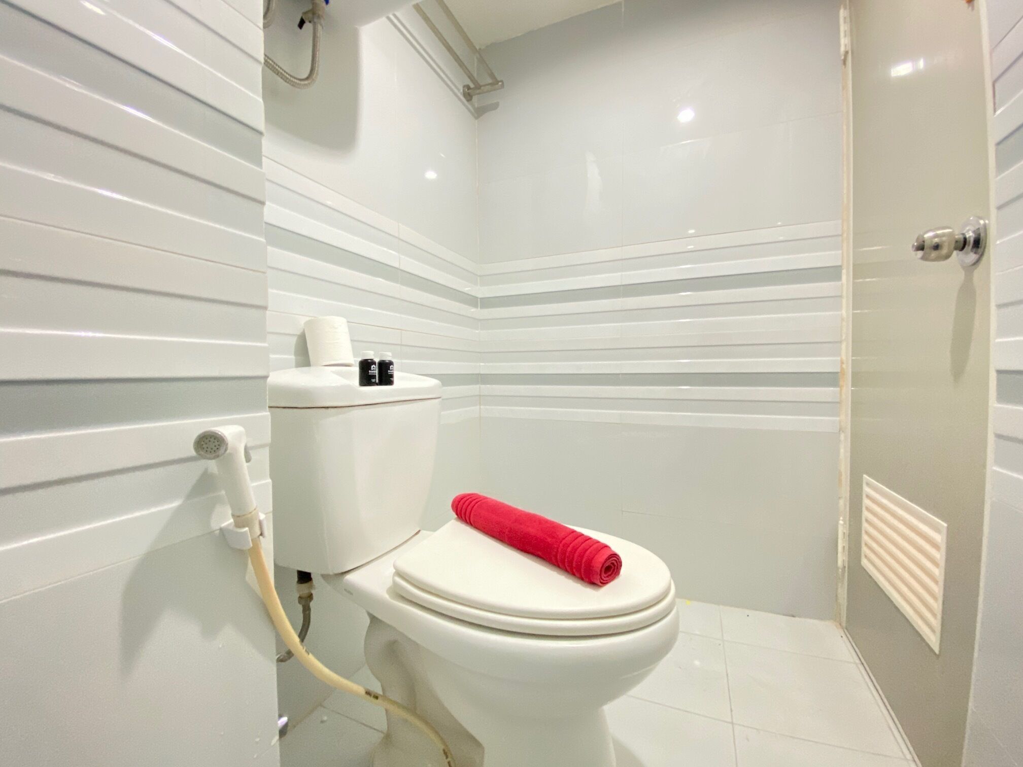Une salle de bain moderne avec des toilettes blanches, une serviette rouge posée sur le siège et un espace douche.