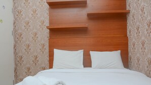 A neatly made bed with white linens and pillows, a wooden headboard, and patterned wallpaper. - Modern 2BR Apartment @ Springlake Summarecon (Bekasi)