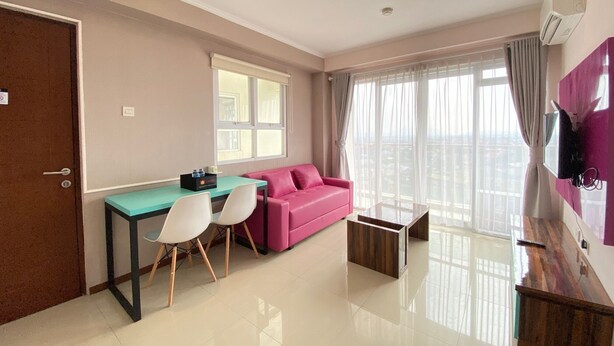 A modern living room with a sofa, a dining table with chairs, a small coffee table, and a TV mounted on the wall. - Modern & Cozy 2BR at Gateway Pasteur Apartment (Cimahi)