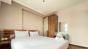 A hotel room with a large bed, a wooden headboard, a mirror, a desk with a chair, and a wardrobe. - Modern & Cozy 2BR at Gateway Pasteur Apartment (Cimahi)