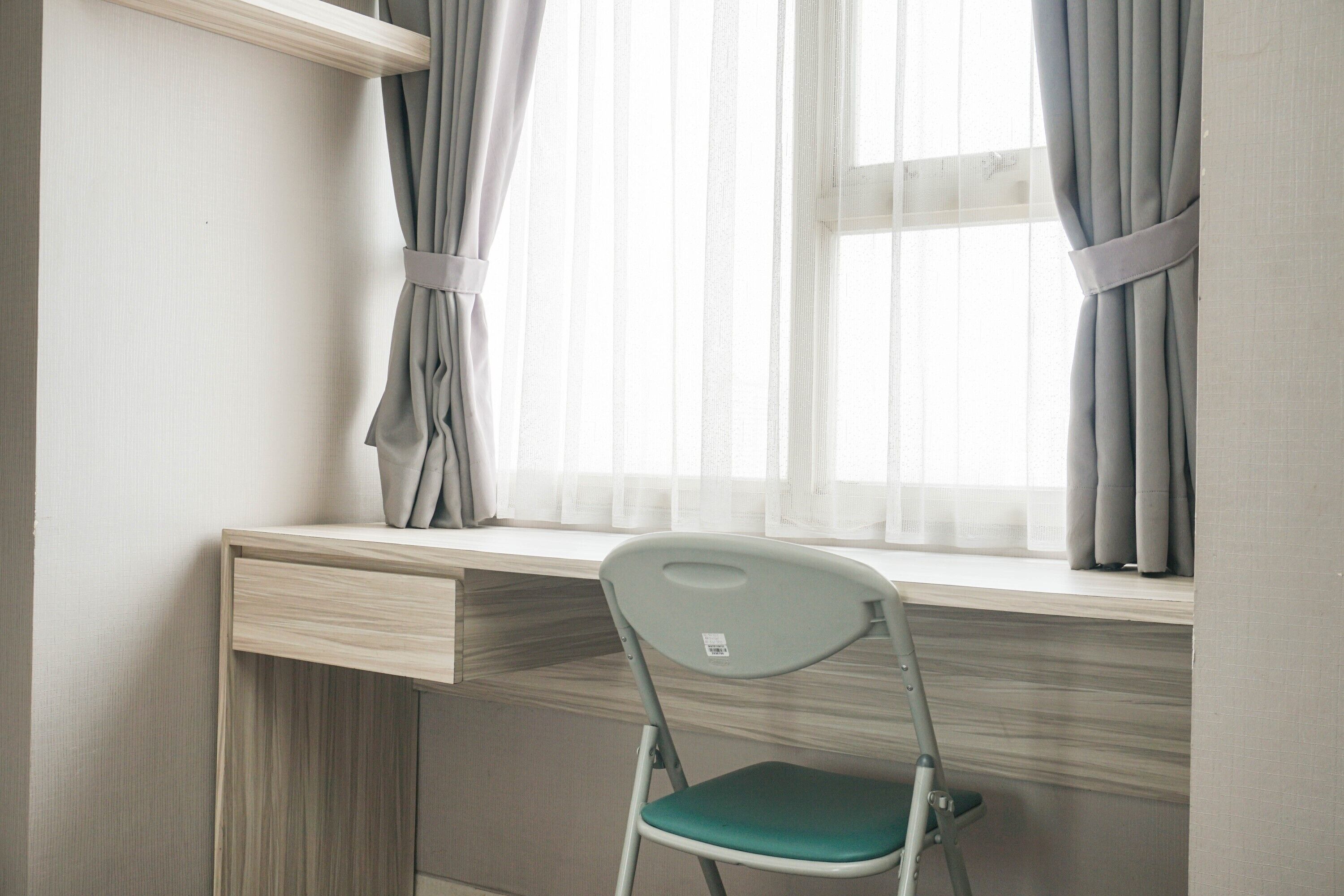 Un escritorio con una silla, una ventana con cortinas y una pared de color claro.
