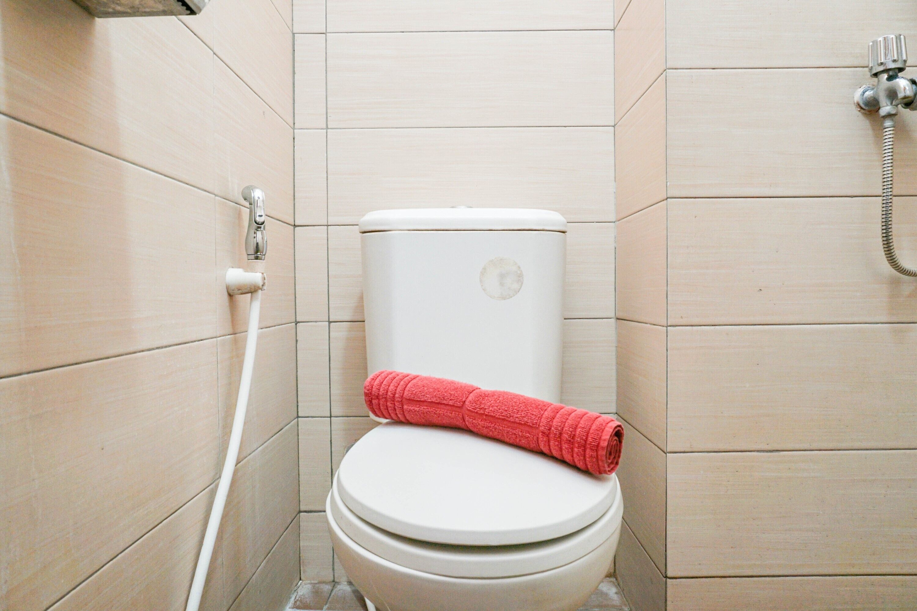 Un baño pequeño y limpio con inodoro, cabezal de ducha y una toalla sobre el asiento.