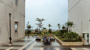 A playground with a climbing structure and a wheelchair-accessible play area, surrounded by a checkered pavement and greenery. - Simply Studio Room Apartment Margonda Residences 5 (Depok)