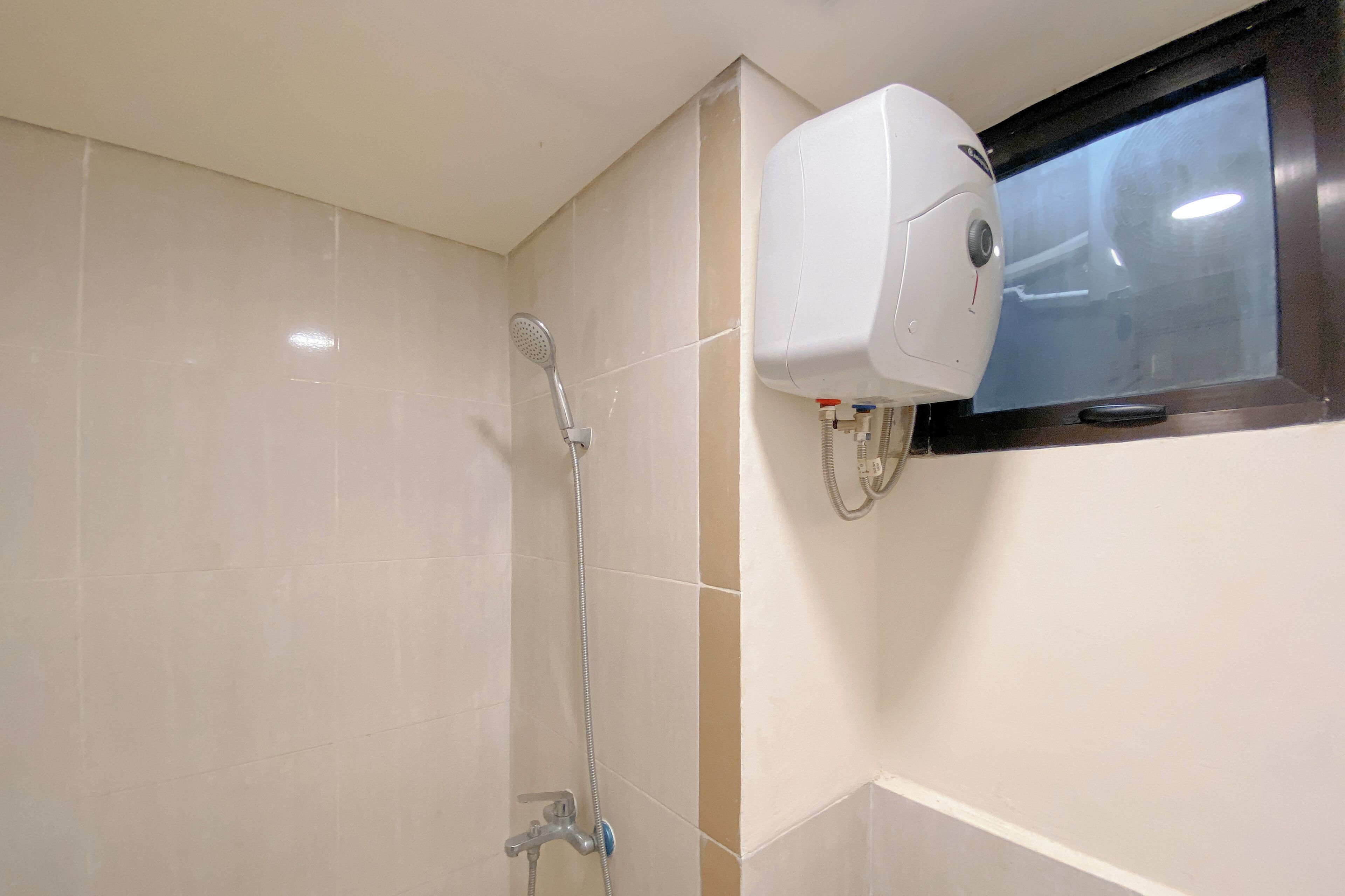 A bathroom with a shower, a handheld showerhead, and a soap dispenser mounted on the wall.