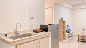 Moderni keittiö, jossa on ruostumattomasta teräksestä valmistettu pesuallas, pienikokoinen jääkaappi ja pieni televisio puisen jalustan päällä.