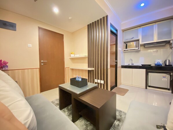 A modern living room with a sofa, a coffee table, and a small kitchen area with a microwave and cabinets.