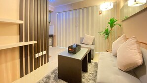 A modern living room with a sofa, a coffee table, and a decorative plant. There is a sliding door with vertical blinds and a ceiling light fixture. - Cozy and Stylish 1BR Apartment at Gateway Pasteur (Cimahi)