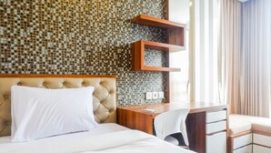 Una camera d'hotel con una testiera trapuntata, una scrivania in legno con cassetti, una sedia bianca e una parete decorata.