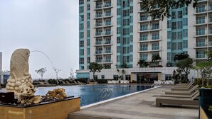 Una piscina con gradoni che vi conducono, circondata da sdraio e un grande edificio sullo sfondo.