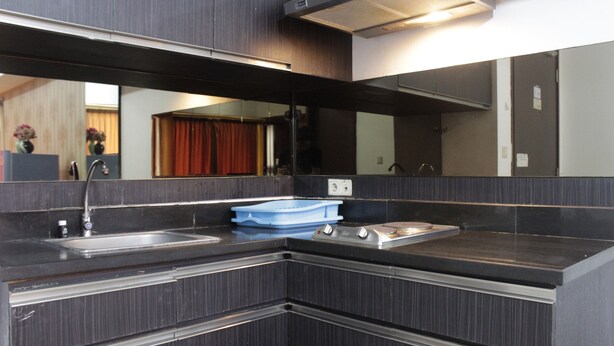 A modern kitchen with dark cabinetry, a stainless steel sink, and a blue dish rack. - Deluxe & Comfy 2BR at Braga City Walk Apartment (Bandung)
