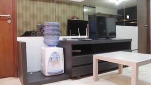 A modern living room with a dark wood entertainment center, a flat-screen TV, a water dispenser, and a wooden coffee table. - Deluxe & Comfy 2BR at Braga City Walk Apartment (Bandung)
