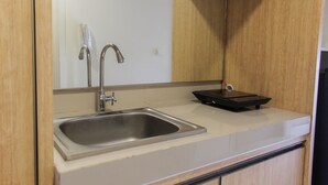 Una cocina con un lavamanos de acero inoxidable, un grifo y una pequeña bandeja negra sobre la encimera.
