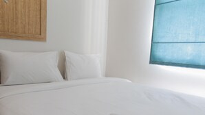 Una cama bien hecha con sábanas y almohadas blancas, un cabecero de madera y una ventana con vistas azules.