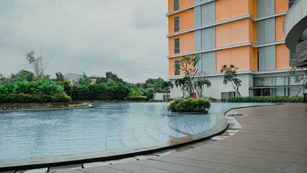 A modern building with a curved pool and a wooden deck. - New Furnish and Homey 1BR Apartment at Pejaten Park Residence (Jakarta)