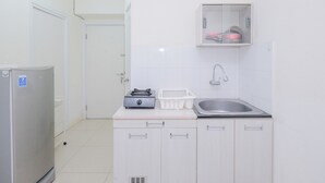 A compact kitchen with a refrigerator, a sink, and a countertop with a dish rack and a kettle. - Cozy and Simply 1BR Green Pramuka Apartment (Jakarta)