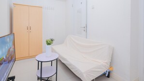 A small room with a wooden wardrobe, a white door, a small round table with a potted plant, and a covered sofa. - Cozy and Simply 1BR Green Pramuka Apartment (Jakarta)