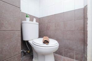 A bathroom with a toilet, a small potted plant, and a towel on the seat. - Cozy and Simply 1BR Green Pramuka Apartment (Jakarta)