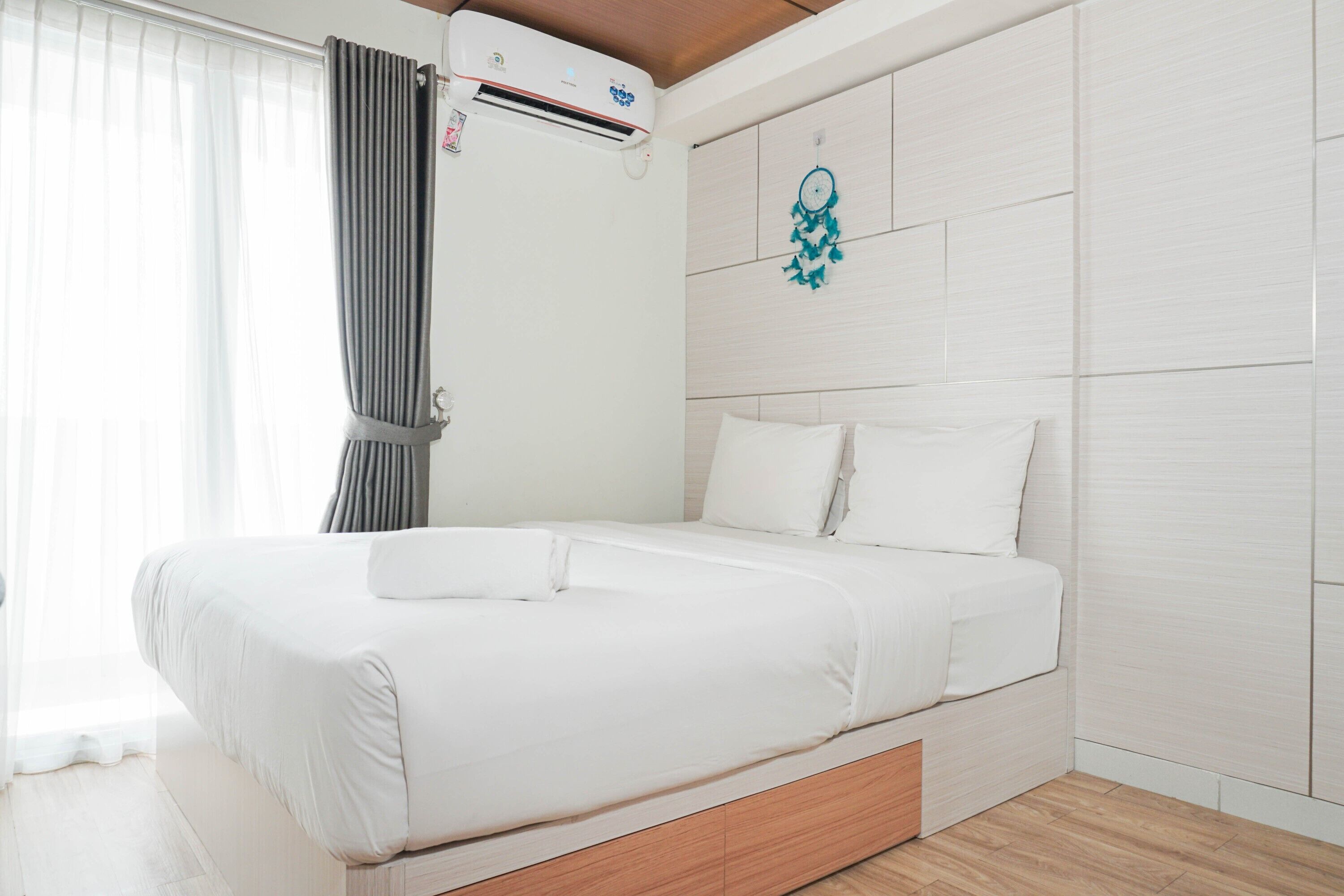 A modern hotel room with a large bed, white linens, a wooden headboard, and an air conditioning unit.