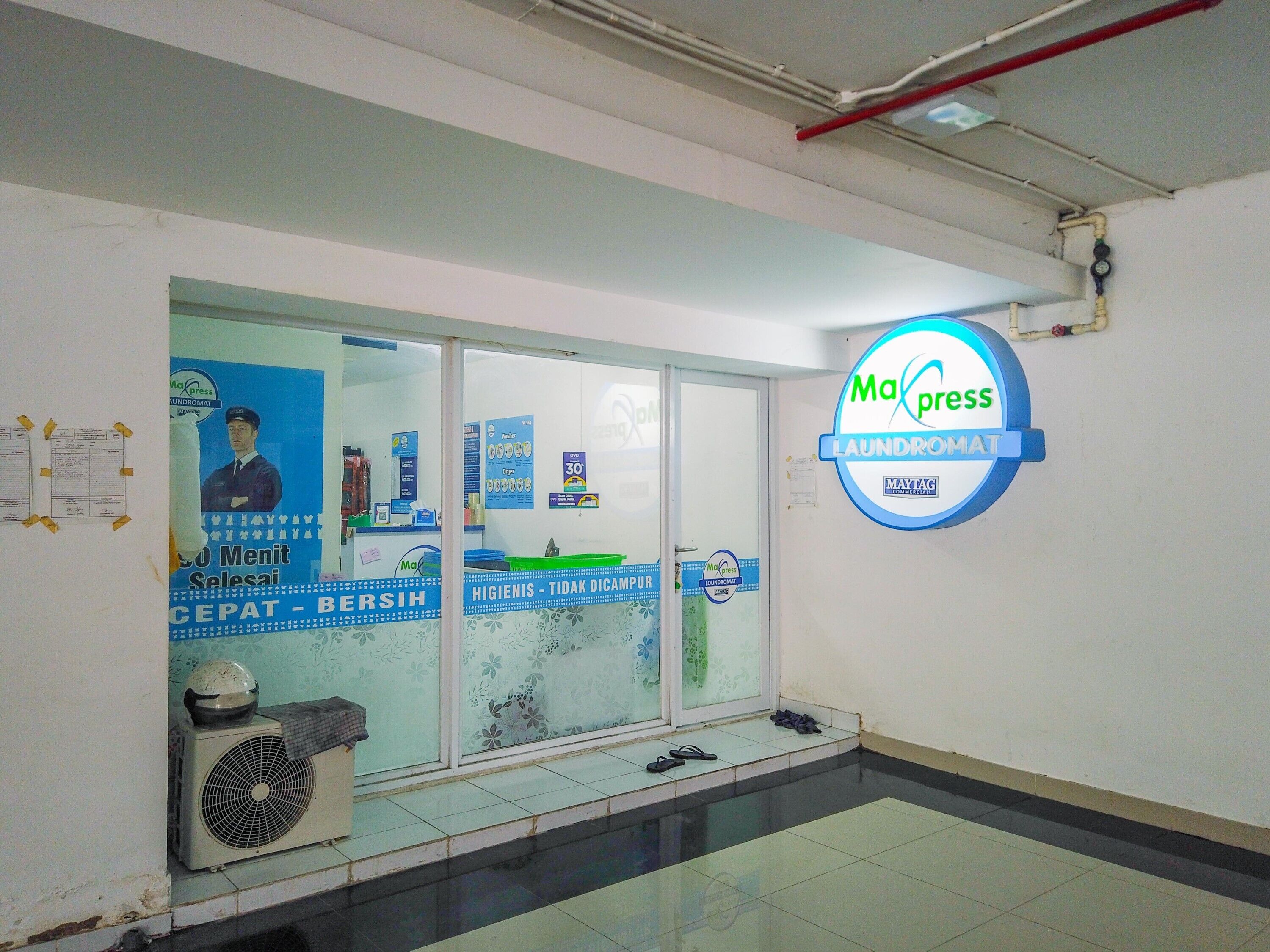 A laundromat with a large sign, glass doors, and a fan outside.