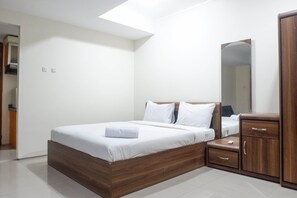 A modern bedroom with a wooden bed frame, white bedding, a small bedside table, and a wardrobe. - Best Value & Spacious Studio Room Apartment at High Point Serviced (Surabaya)