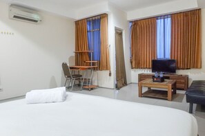 A hotel room with a bed, a desk with a chair, a television, and curtains. - Best Value & Spacious Studio Room Apartment at High Point Serviced (Surabaya)